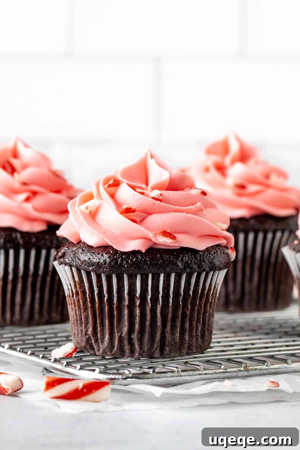 Crimson Cane Cocoa Delights 3 Chocolate cupcakes with delicate pink peppermint frosting cooling on a wire rack.