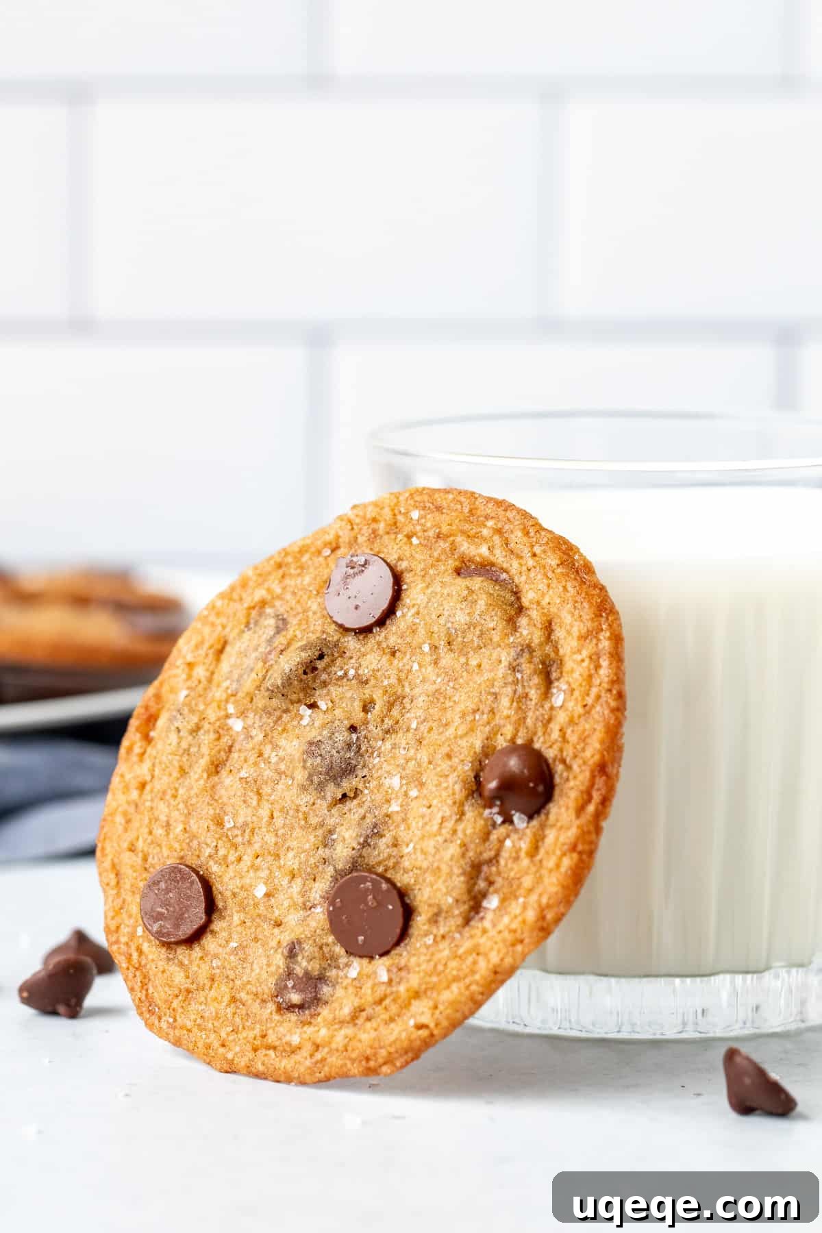 A single crispy chocolate chip cookie leaning against a glass of milk, showcasing its delicate texture and golden-brown hue.