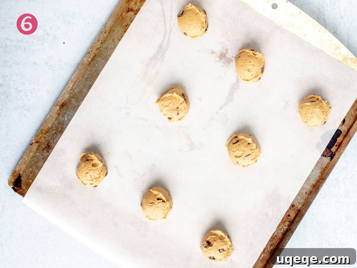 A lined cookie tray with evenly spaced, unbaked chocolate chip cookie dough balls, ready to go into the oven.