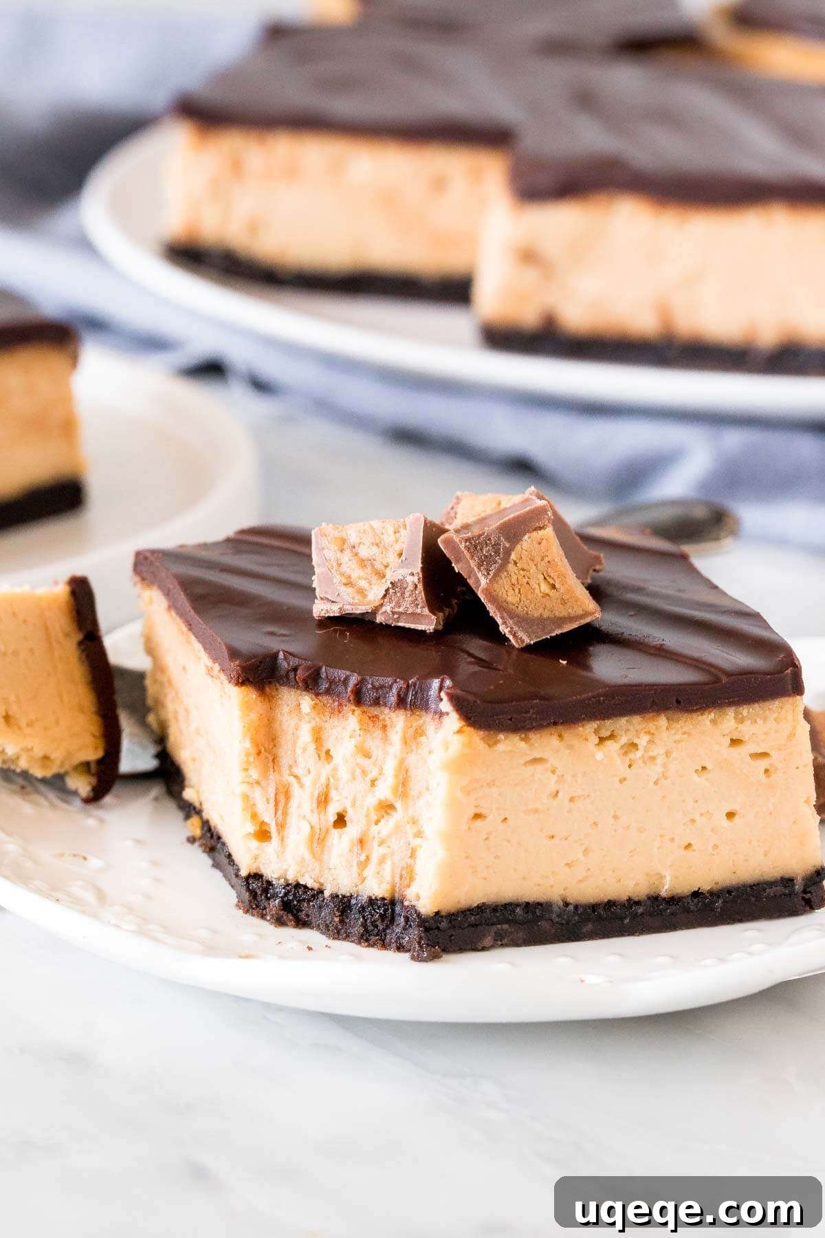 Slice of peanut butter cheesecake bars topped with chocolate and peanut butter cups. 