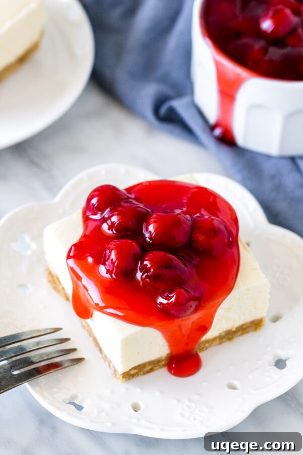 Luscious Chilled Cherry Bars 5 A perfectly portioned square of no-bake cheesecake bar on a white plate, topped with a generous spoon of bright red cherry pie filling.