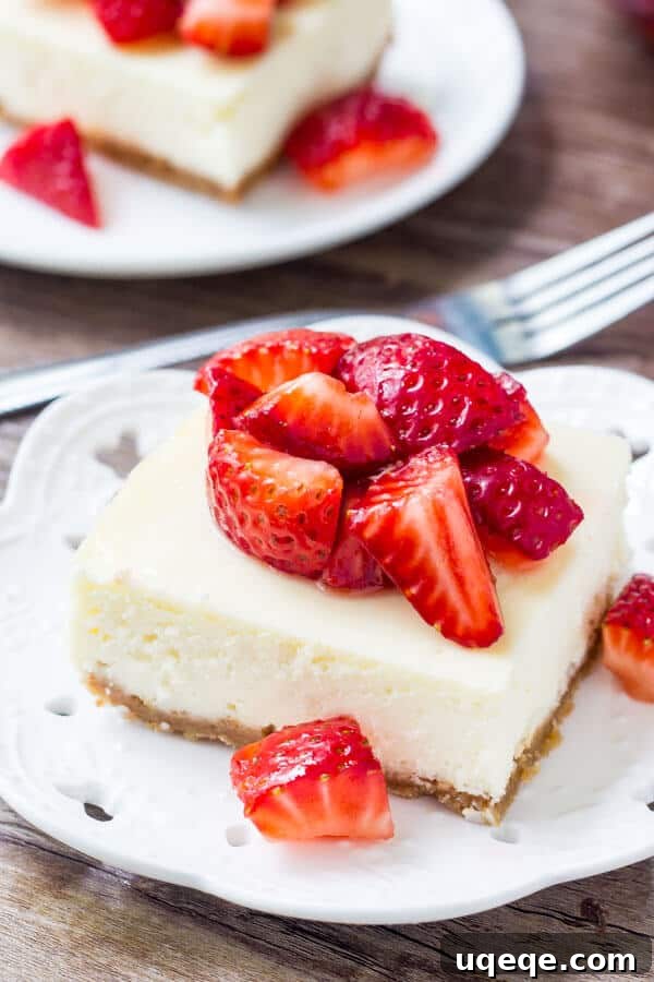 Strawberry Graham Bliss Bars 2 Cheesecake bar topped with chopped strawberries on a white plate. Fork and second cheesecake bar in the background.