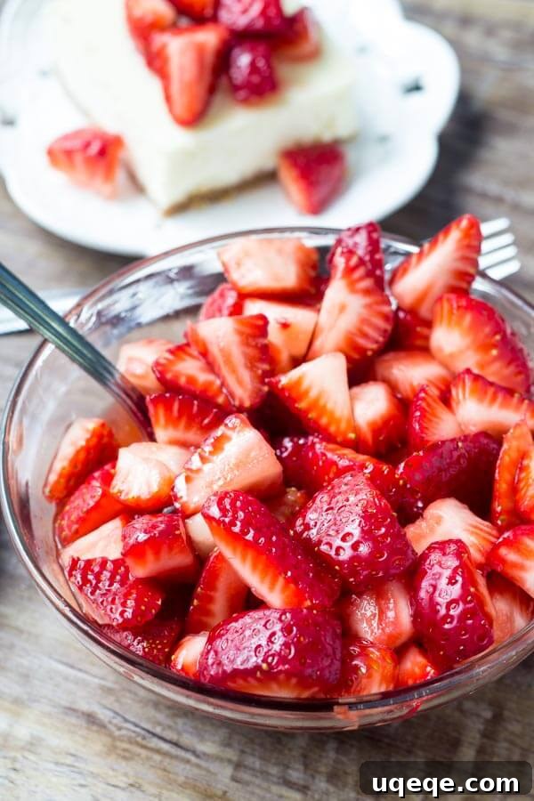 Strawberry Graham Bliss Bars 4 Bowl of chopped sugared strawberries with slice of cheesecake bars in the background.