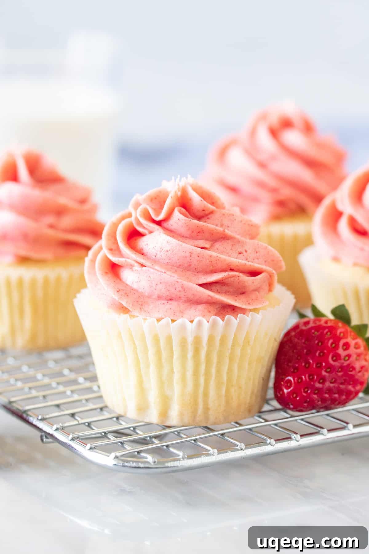 Moist vanilla cupcakes with fresh strawberry buttercream on a cooling rack, showcasing their delicate crumb and creamy pink frosting.