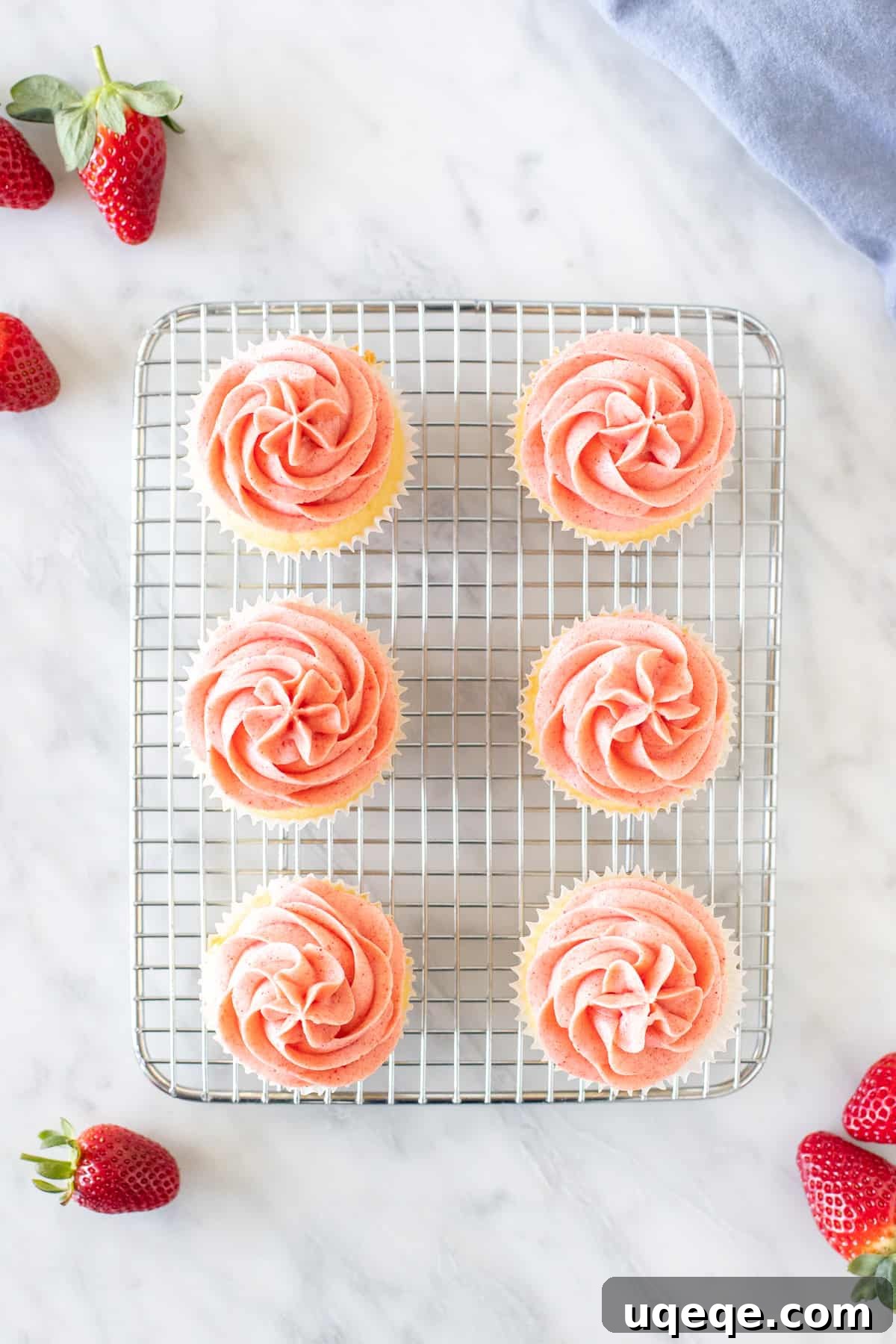Six beautifully frosted vanilla cupcakes with pink strawberry buttercream arranged neatly on a wire cooling rack, ready to be enjoyed.