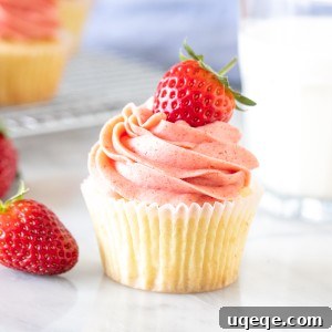 A delicious vanilla cupcake topped with creamy pink strawberry frosting, served alongside a glass of fresh milk.