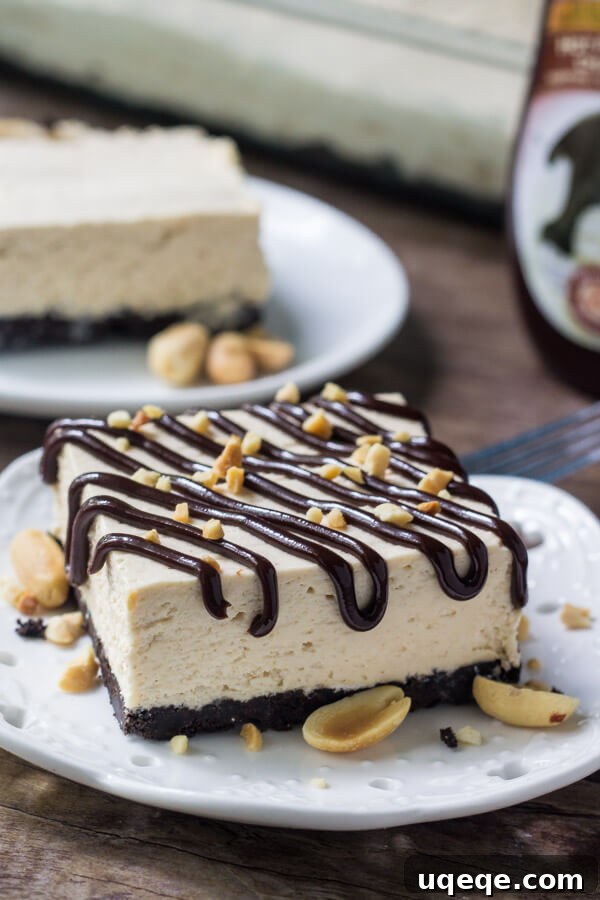 Peanut Butter Crunch Drumstick Ice Cream Cake 4 A side view of a perfect slice of drumstick cake on a white plate, ready to be enjoyed. In the background, there's a fork, a bottle of hot fudge sauce, another delicious slice, and the full pan of drumstick cake, showcasing its appeal.