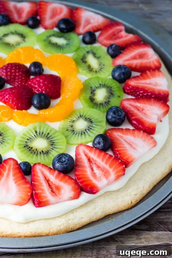 Vibrant Sugar Cookie Fruit Pizza 2 Whole sugar cookie fruit pizza topped with strawberries, blueberries, kiwis and mandarin oranges in it's pizza pan.