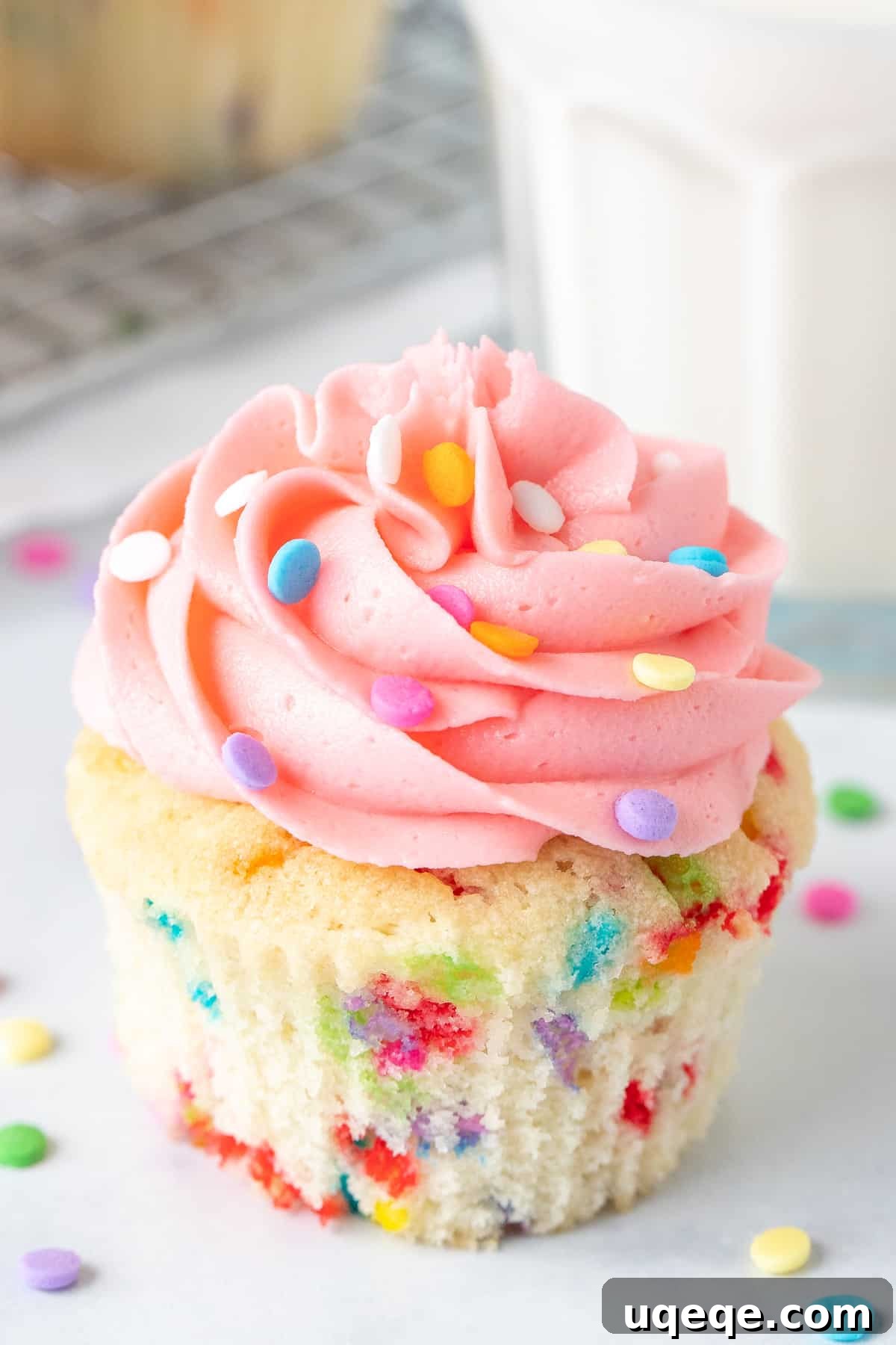 Funfetti cupcake with pink frosting and glass of milk