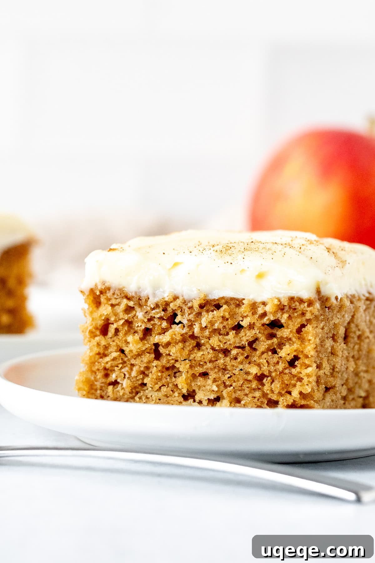Orchard Spice Cake with Cream Cheese Cloud 2 A square slice of incredibly moist apple spice cake topped with generous cream cheese frosting, ready to be enjoyed.