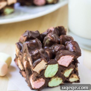 One peanut butter chocolate confetti square on a piece of wax paper. Glass of milk and plate of squares in the background.