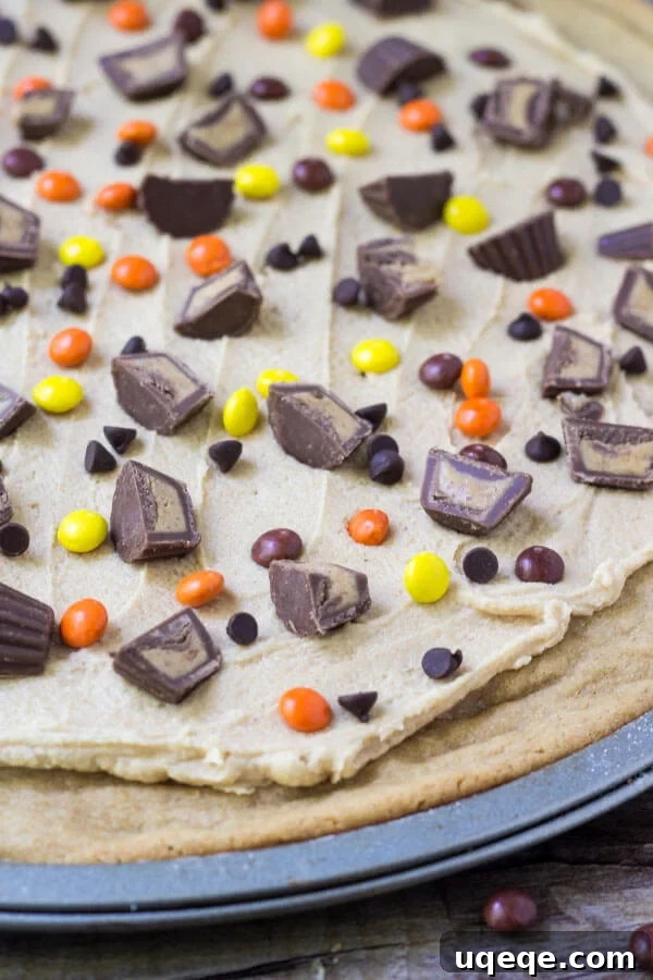 Overhead shot of full peanut butter cookie pizza on it's pizza pan. With peanut butter frosting & peanut butter candies