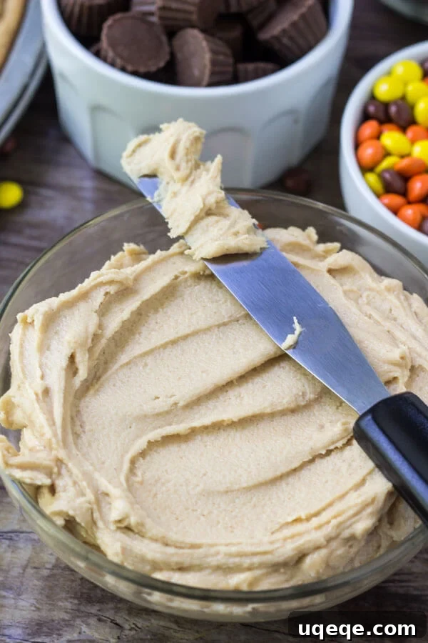 Bowl of creamy peanut butter frosting with bowls of Reese's Pieces and peanut butter cups in the background.