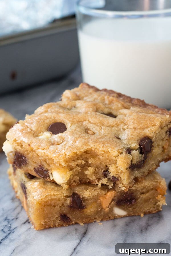 Triple Chocolate Chip Dream Bars 2 Stack of 2 triple chip cookie bars with a bite taken out of the bar on top. A glass of milk and the pan in the background.