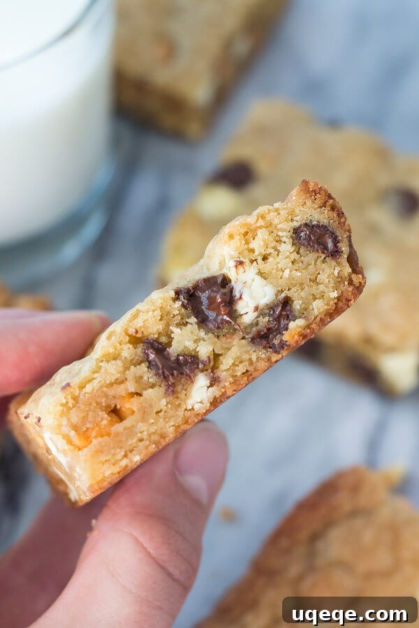 Triple Chocolate Chip Dream Bars 3 Side shot of a hand holding a triple chip cookie bar. Glass of milk and more cookie bars in the background.