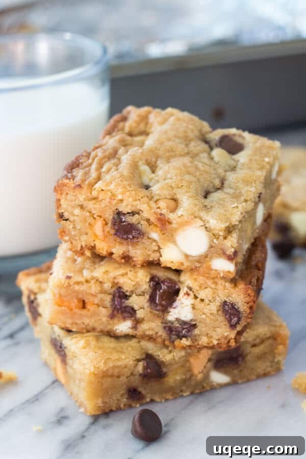 Triple Chocolate Chip Dream Bars 5 Side shot of 3 stacked triple chip cookie bars with a glass of milk and the cookie bar pan in the background.