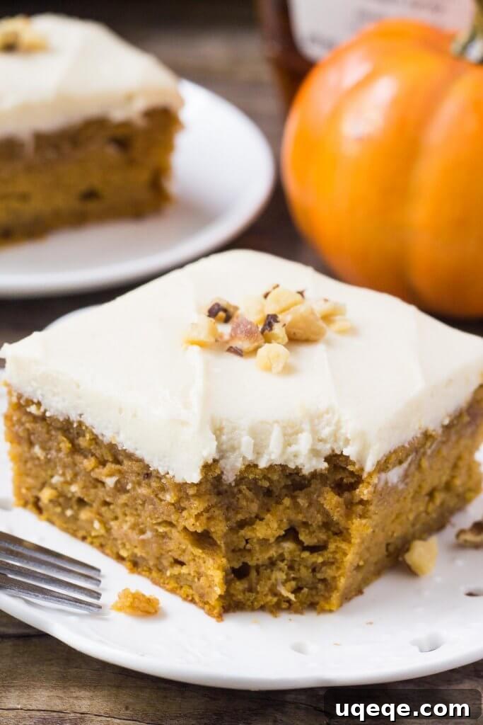 Golden Maple Pumpkin Cake 4 A close-up view of the corner of a slice of pumpkin cake with maple frosting on a plate, showing the layered texture of the moist cake and the thick, smooth frosting. The setting is warm and inviting, perfect for a fall dessert.
