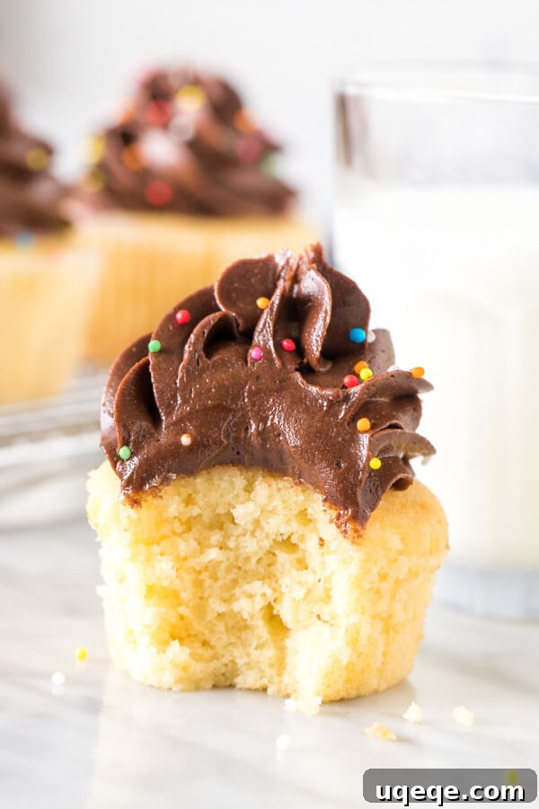 Golden Cupcakes with Velvety Chocolate Frosting 4 A perfectly frosted yellow cupcake with a small bite taken out, revealing its moist, golden interior.