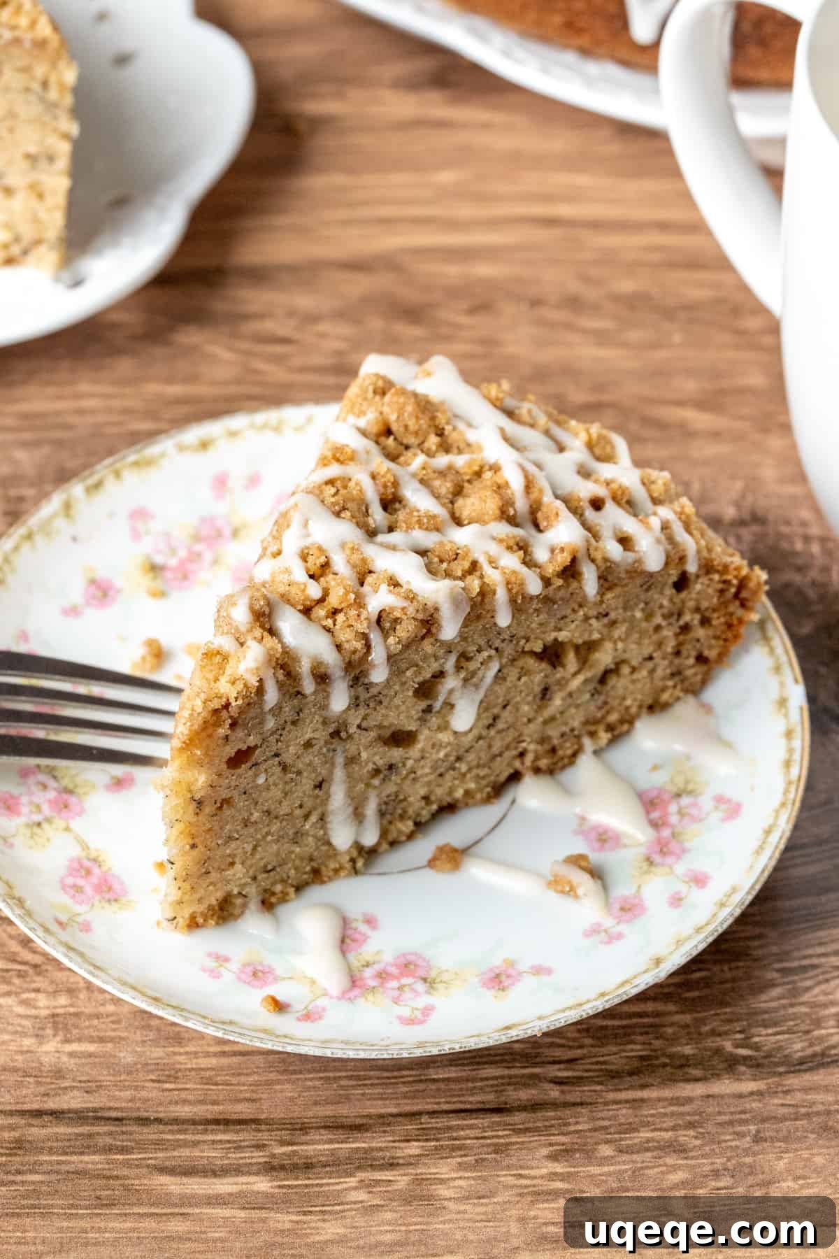 Slice of perfectly baked banana coffee cake, generously drizzled with a smooth vanilla glaze, invitingly placed on a white plate
