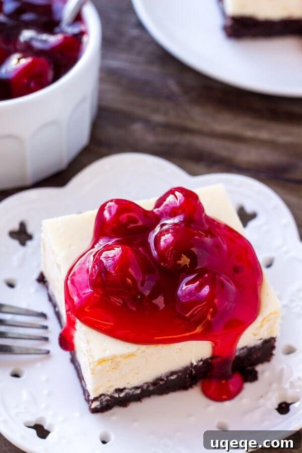 An overhead view of a luscious slice of brownie cheesecake bars, adorned with bright red cherries. A bowl of cherry topping sits invitingly in the soft-focus background.