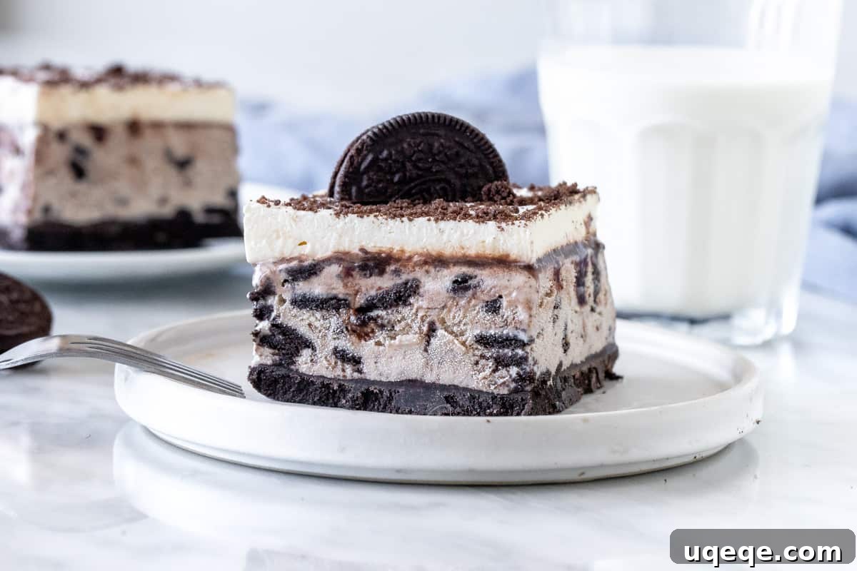 A close-up of a single slice of cookies and cream ice cream cake, showcasing the distinct layers of crust, ice cream, fudge, and whipped topping.