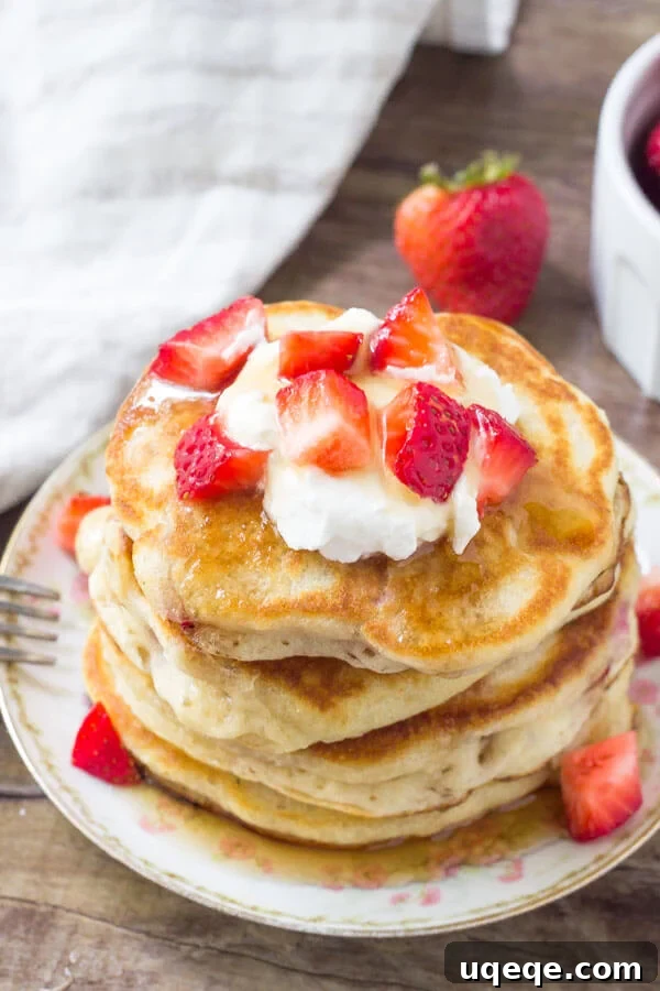 Strawberry pancakes stacked high, topped with fresh whipped cream, more strawberries, and a generous drizzle of maple syrup for a perfect breakfast or dessert.