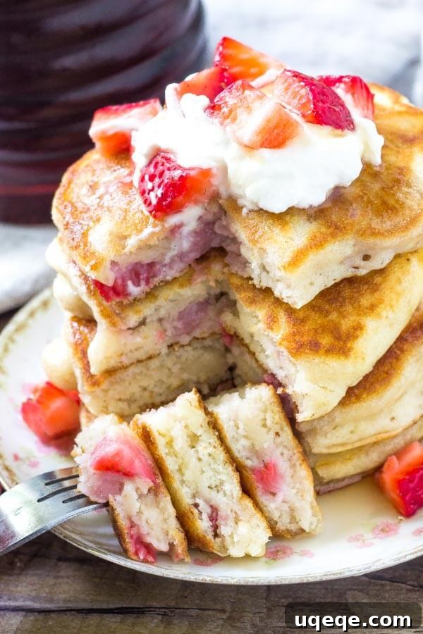 Beautifully stacked fluffy strawberry pancakes, generously filled with pieces of fresh strawberries, making them perfect for any breakfast or dessert occasion.