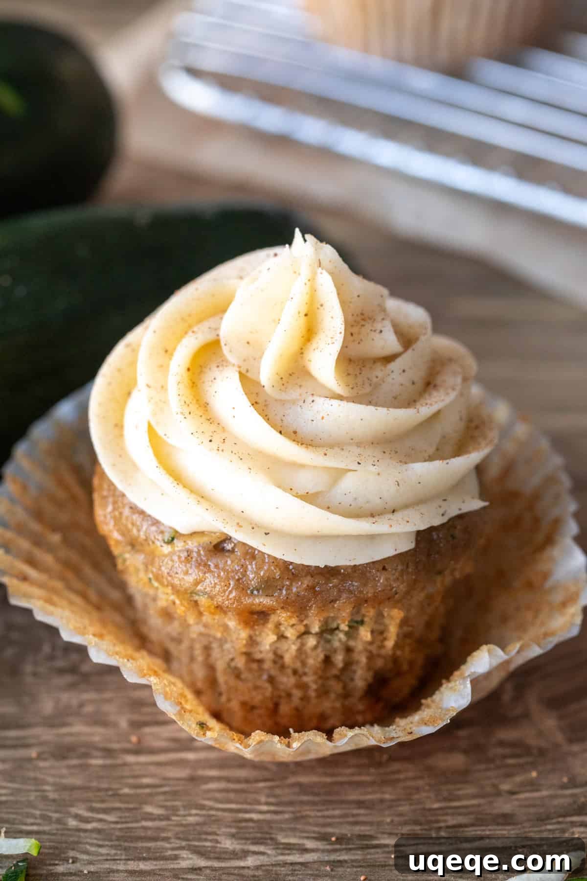Moist Zucchini Delights with Creamy Dream Frosting 2 A beautifully frosted zucchini cupcake with cinnamon cream cheese frosting, with the cupcake paper gently peeled back, showcasing its moist texture.