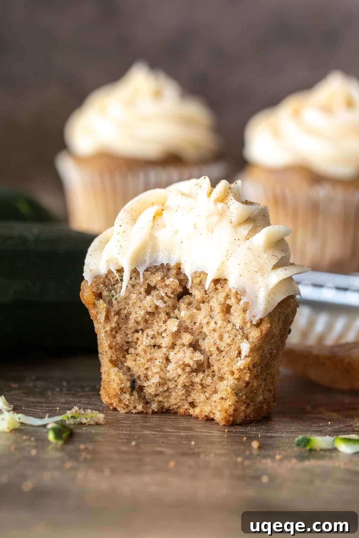 Moist Zucchini Delights with Creamy Dream Frosting 8 A zucchini cupcake with a bite taken out, revealing the moist spice cake interior and the rich cinnamon cream cheese frosting.