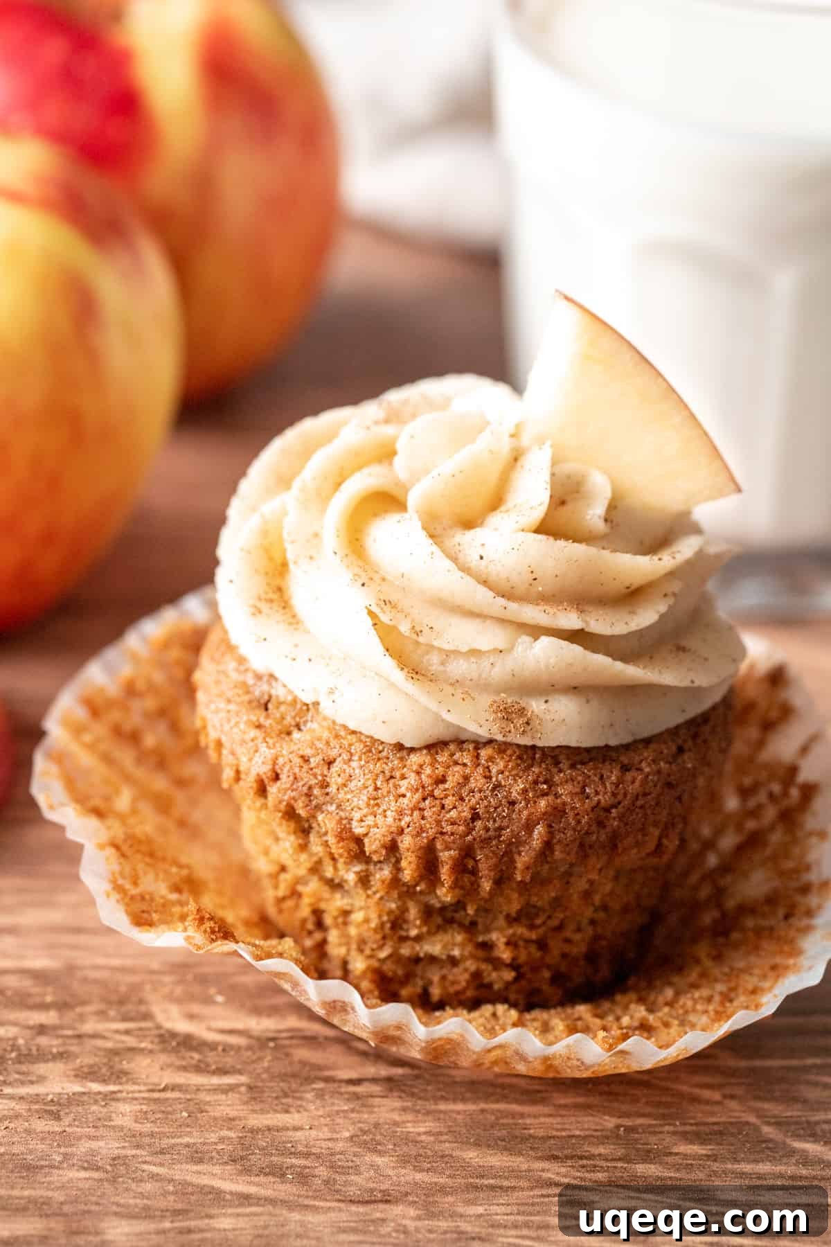 Delicious apple cupcake with cream cheese frosting, garnished with a fresh apple slice, alongside a glass of milk.