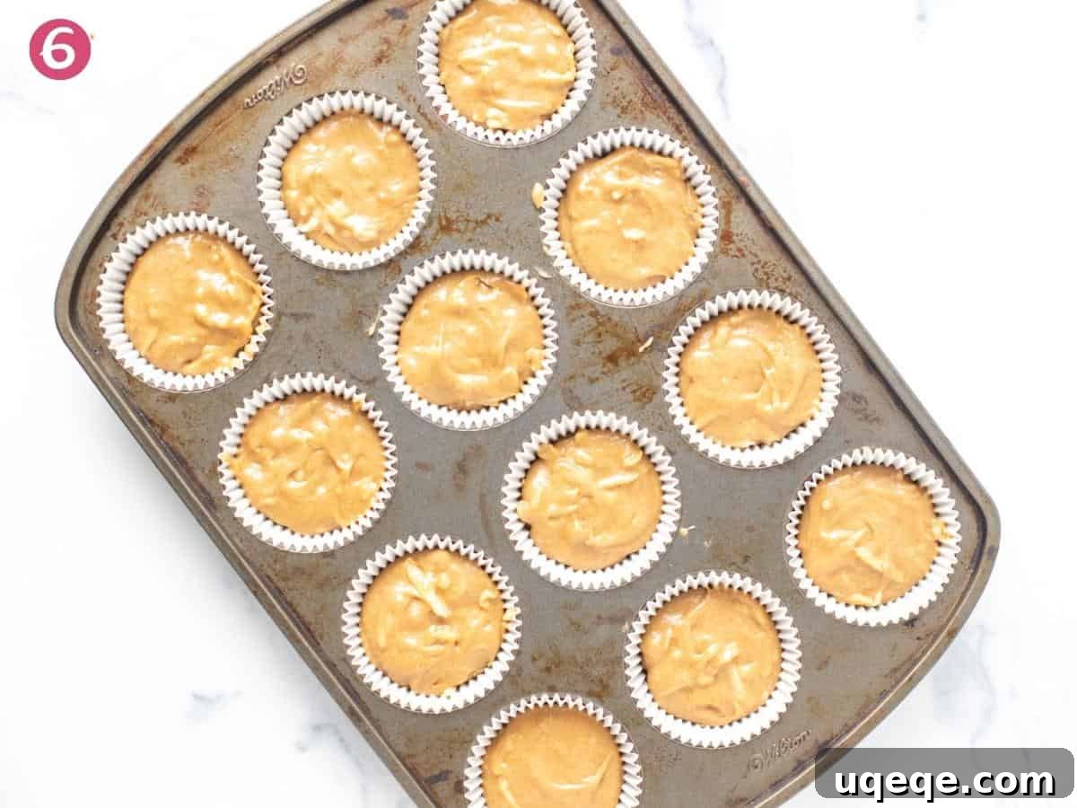 Apple cupcake batter carefully spooned into a muffin tin lined with paper cups, ready for baking.