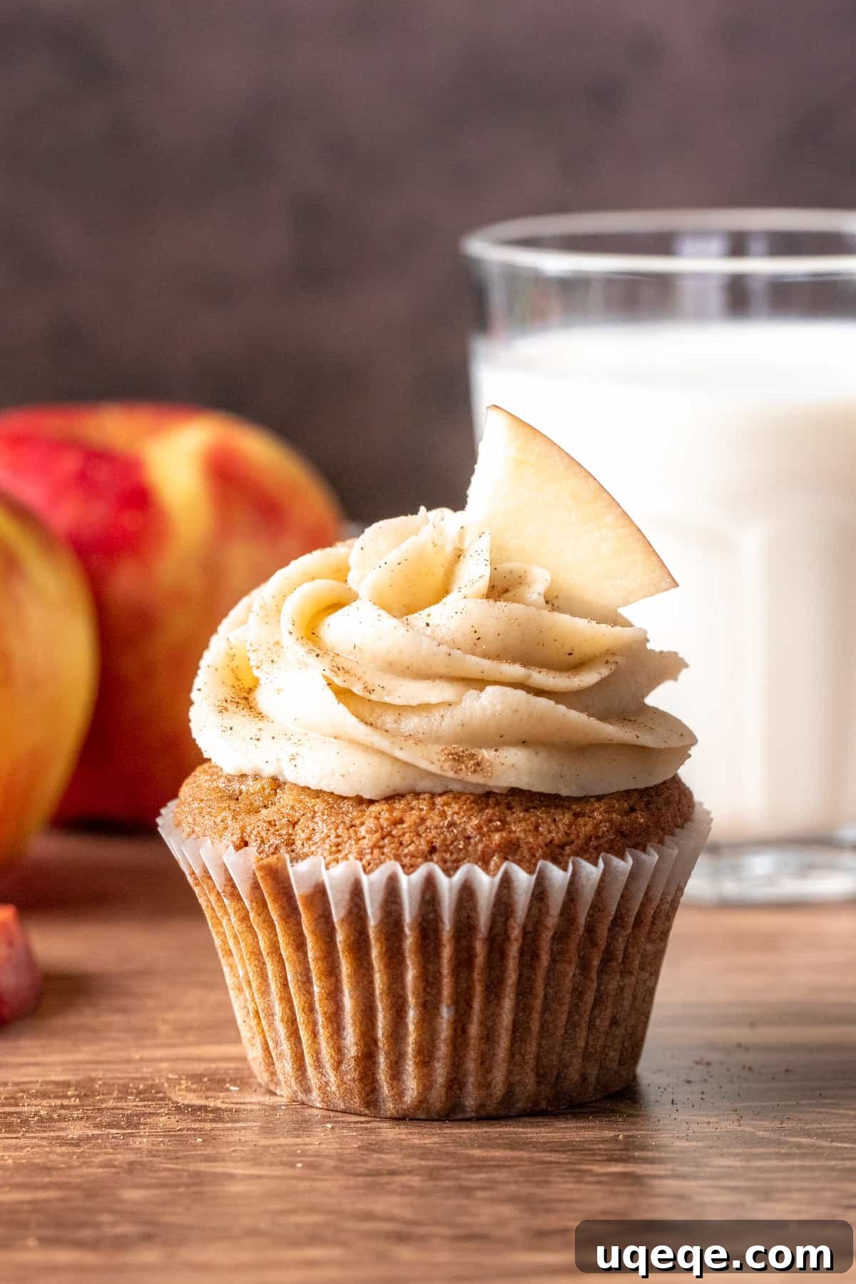 Delicious apple cupcake topped with cinnamon cream cheese frosting, presented with a glass of milk and fresh apples, evoking a cozy fall feeling.