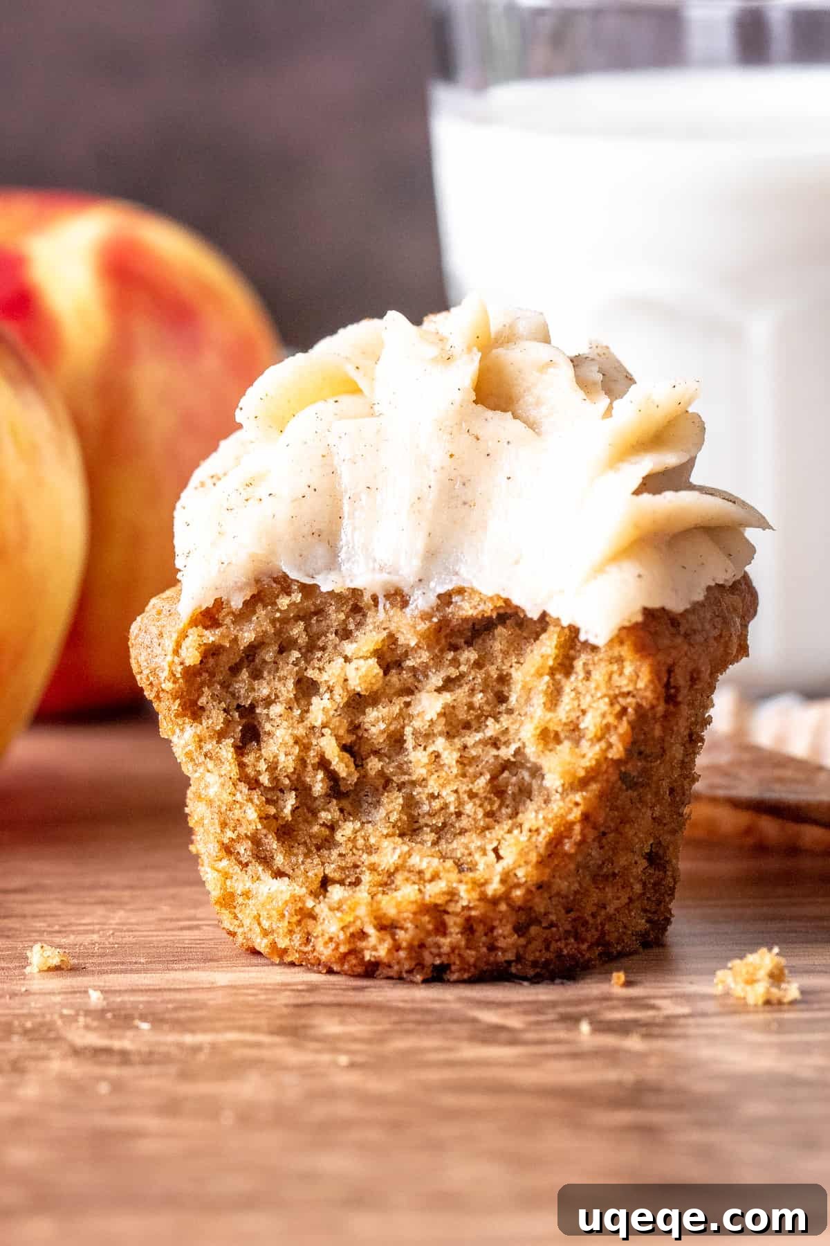 A perfectly baked apple spice cupcake with a bite taken out, revealing its moist interior and delicious texture, topped with cream cheese frosting.