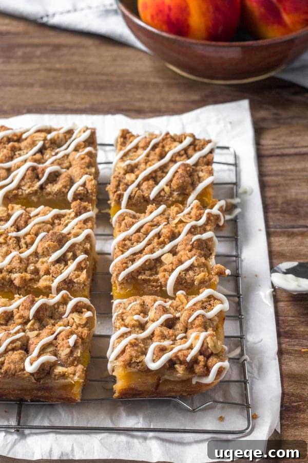 Peachy Crumble Bars 5 A close-up of Peach Pie Bars, highlighting the generous oatmeal crumble topping and a delicate drizzle of vanilla glaze, with visible chunks of baked peaches beneath.