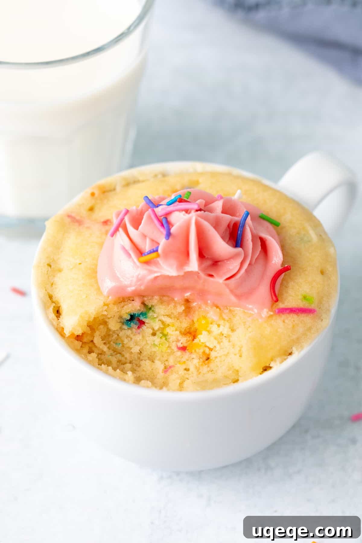 Easy Vanilla Mug Cake 7 Sprinkle mug cake topped with vanilla frosting, with a spoonful taken out