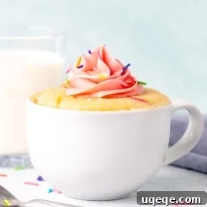 Vanilla mug cake decorated with pink frosting with a glass of milk