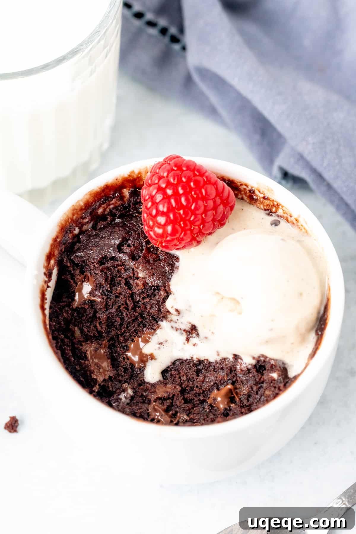 Fudgy Chocolate Mug Treat 2 Delicious chocolate mug cake with a scoop of melting vanilla ice cream and a bite taken out, showing its fudgy interior.
