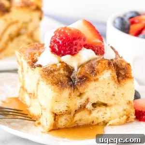 Slice of french toast bake with whipped cream, strawberries and maple syrup on top on a plate.