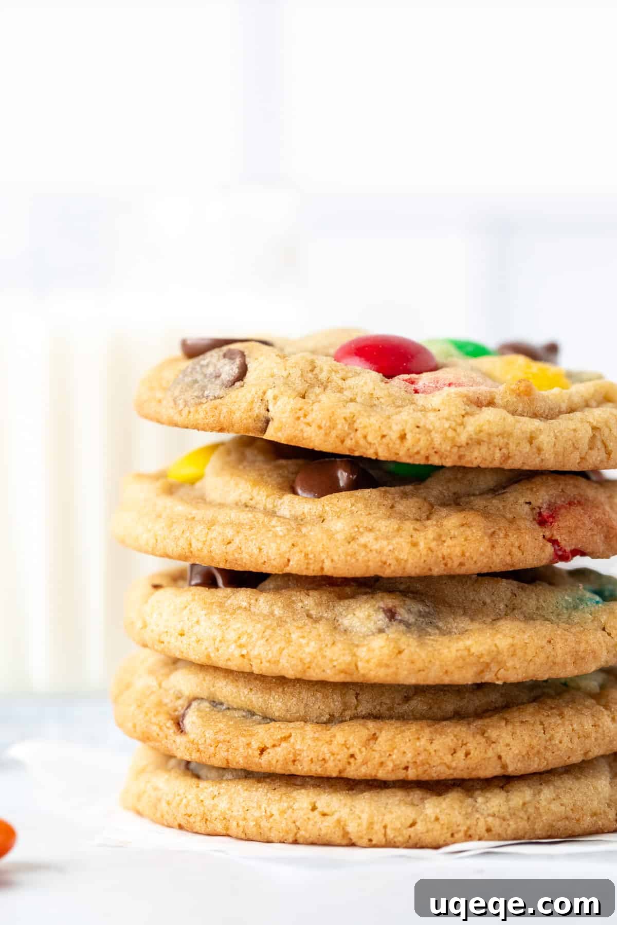 Irresistibly Soft Chewy M and M Cookies 3 Stack of five M&M chocolate chip cookies next to a tall glass of milk, showcasing their vibrant colors and appealing thickness.