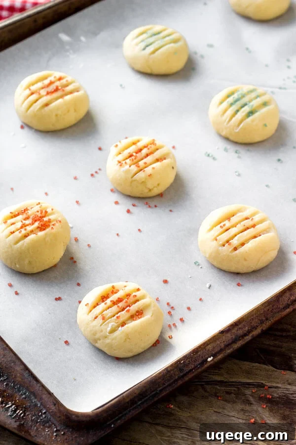 Unbaked whipped shortbread cookie dough balls, pressed with a fork and topped with sprinkles, ready to enter the oven.