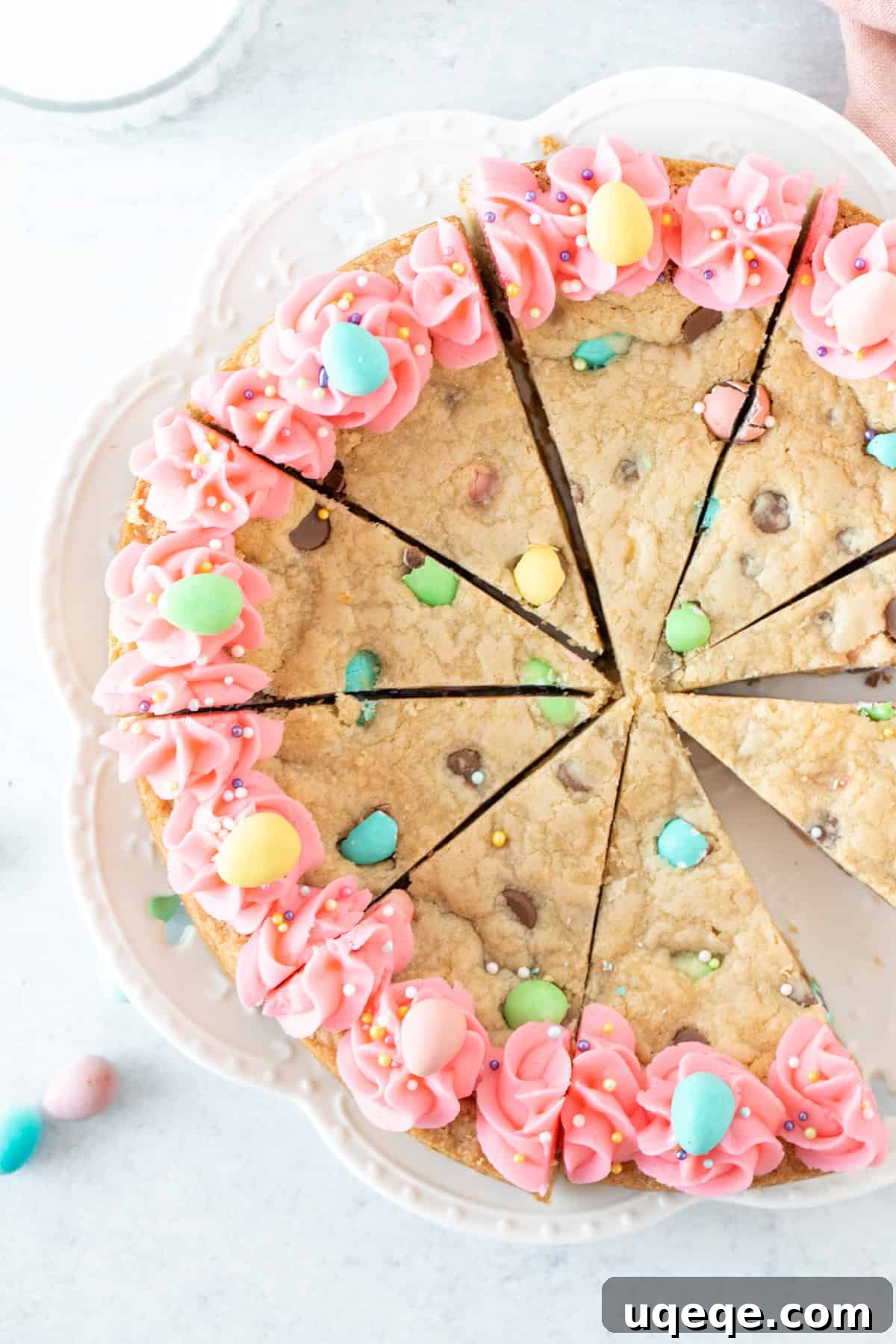 Easter Cookie Cake Delight 2 Easter candy cookie cake, cut into slices on a white plate, showcasing its soft interior and colorful candies.