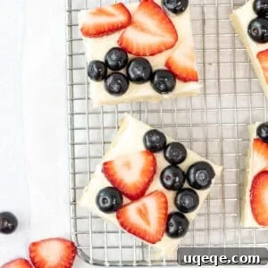 Sugar cookie bars topped with vanilla frosting and fresh berries on a cooling rack