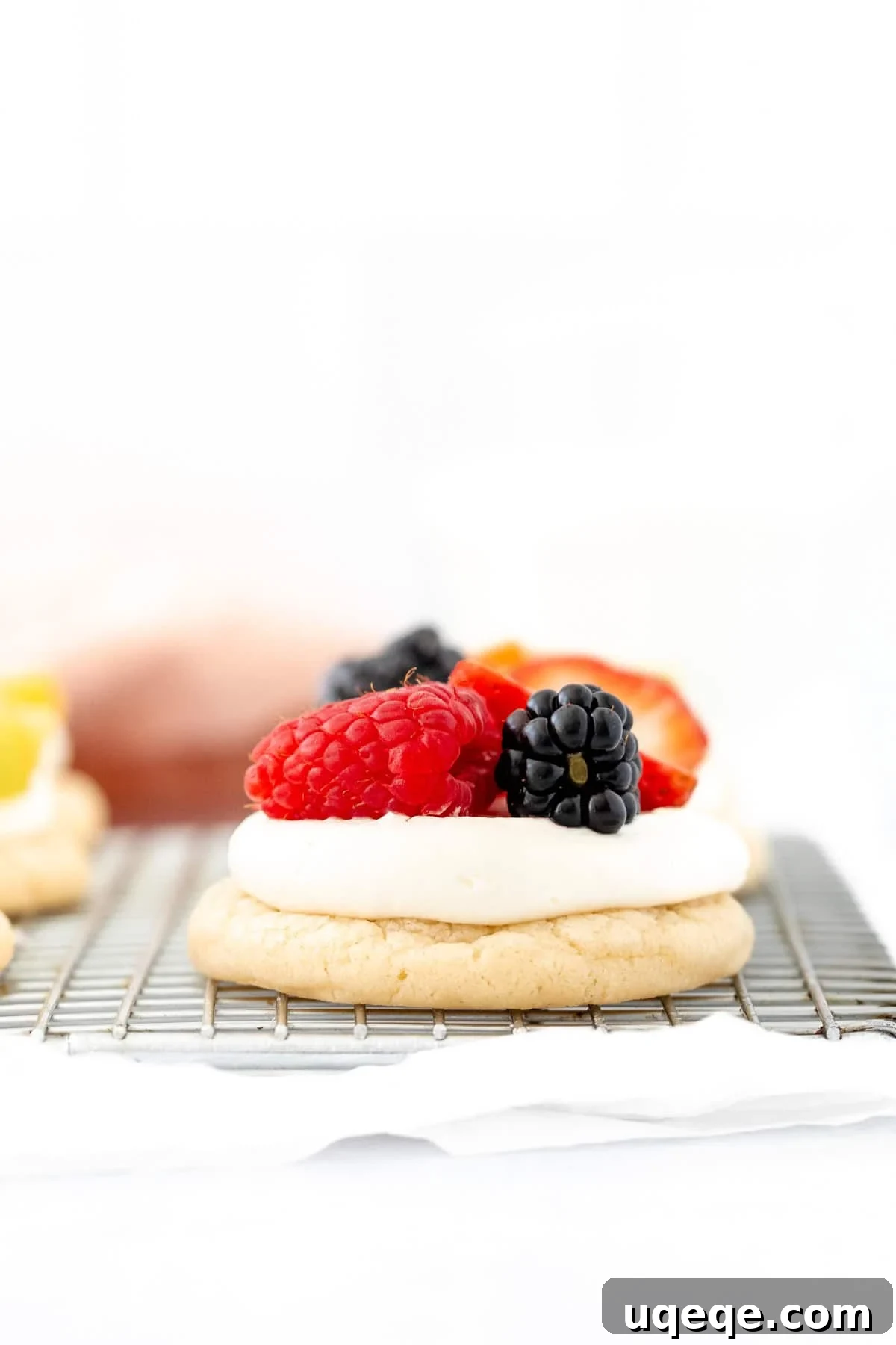 Mini Fruit Pizza Bites with Cream Cheese Frosting 2 mini fruit pizza topped with berries on a cooling rack
