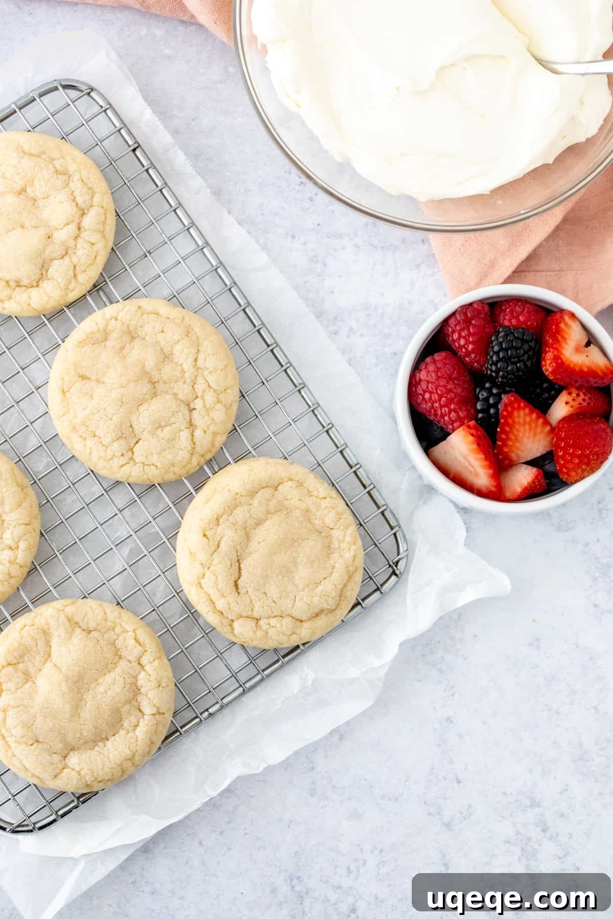 Mini Fruit Pizza Bites with Cream Cheese Frosting 4 sugar cookies on wire rack with a bowl of whipped cream cheese frosting and berries