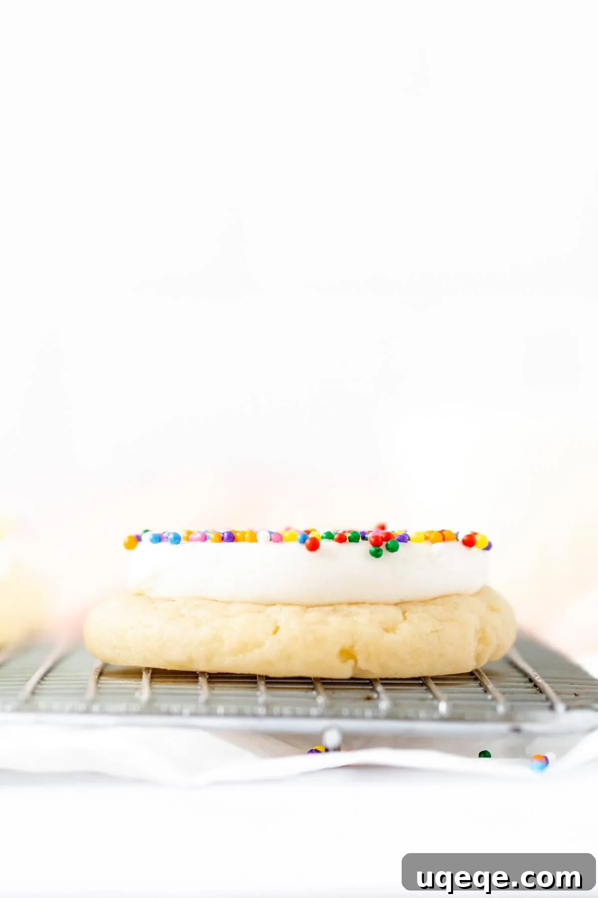 Polka Dot Cake Cookies Recipe for Parties 5 Dot cake cookie on a cooling rack with a thick layer of vanilla frosting and sprinkles on top
