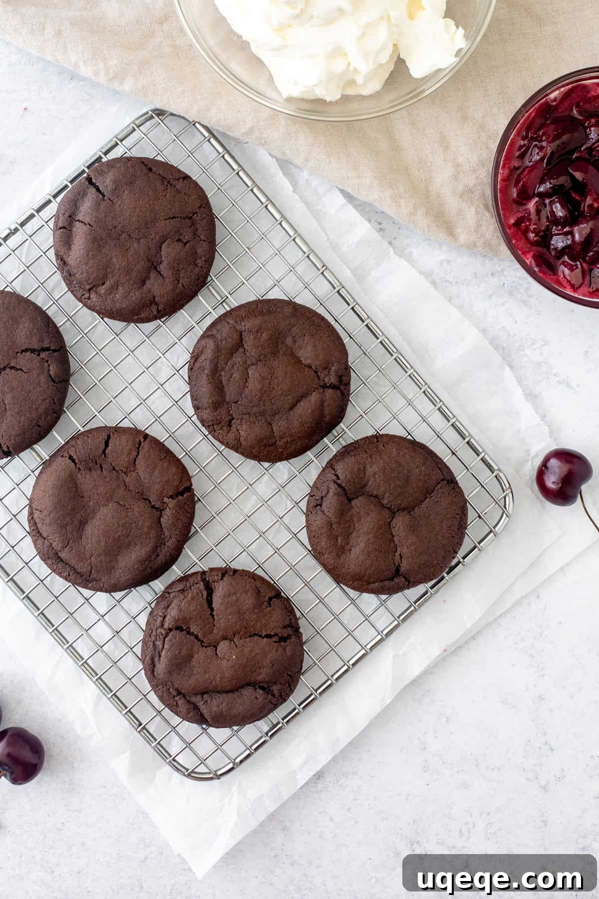 Black Forest Cookies: Chocolate and Cherry Cookie Recipe 5 chocolate cookies on a cooling rack with bowl of whipped cream and bowl of cherry sauce