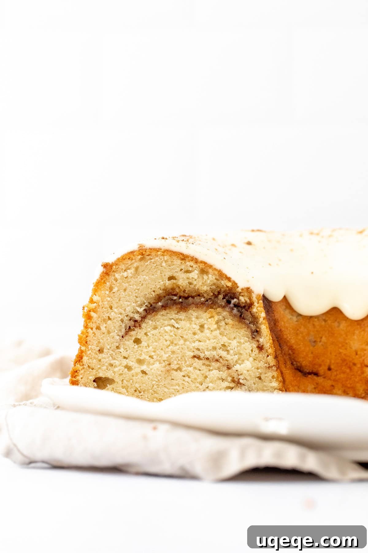 Moist Cinnamon Swirl Bundt Cake Recipe 7 Cinnamon swirl bundt cake with cream cheese icing on a white plate, with slices cut out of the bundt cake